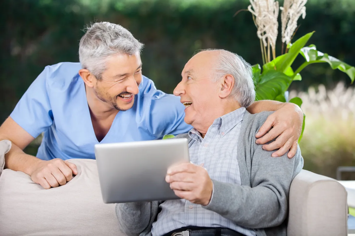 Caregiver and senior man reading together on a tablet